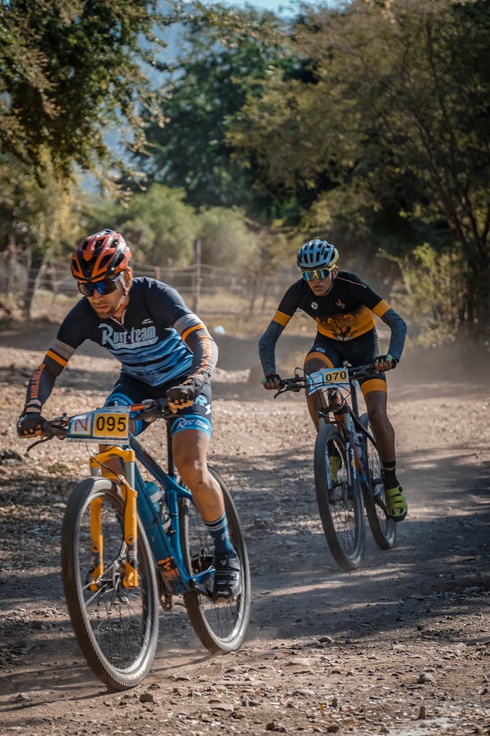Services Two cyclists race fiercely on a dusty mountain trail under clear skies.