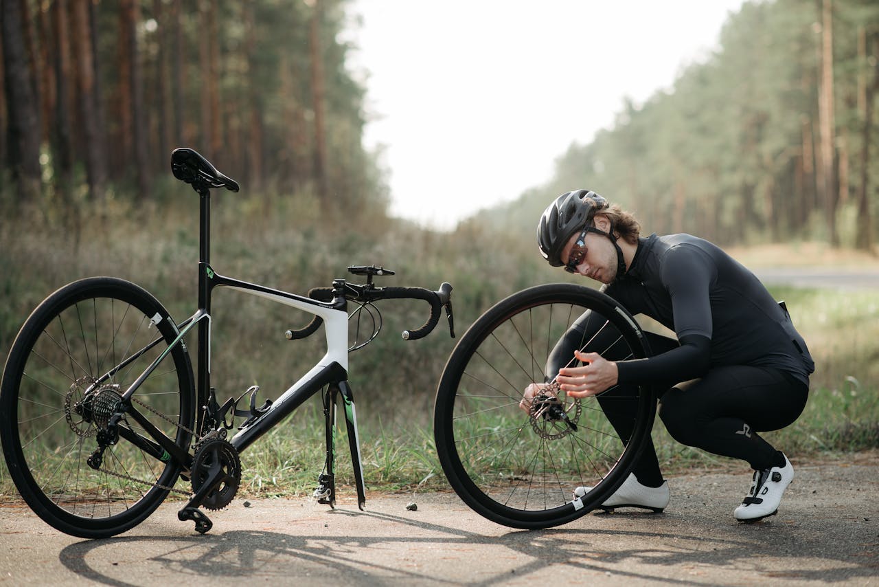 Services Cyclist fixing a road bike wheel on a forest path during daytime.